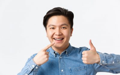 Orthodontics and stomatology concept. Close-up of satisfied asian guy, dental clinic client smiling happy and pointing at his dental braces and showing thumbs-up in approval, recommend.